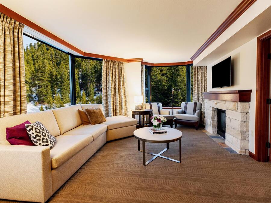 A living room with a sofa, armchairs, a coffee table, a fireplace, and a TV mounted on the wall.