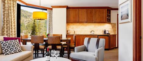 A living room with a sofa, armchairs, a dining table, and a kitchen in the background.