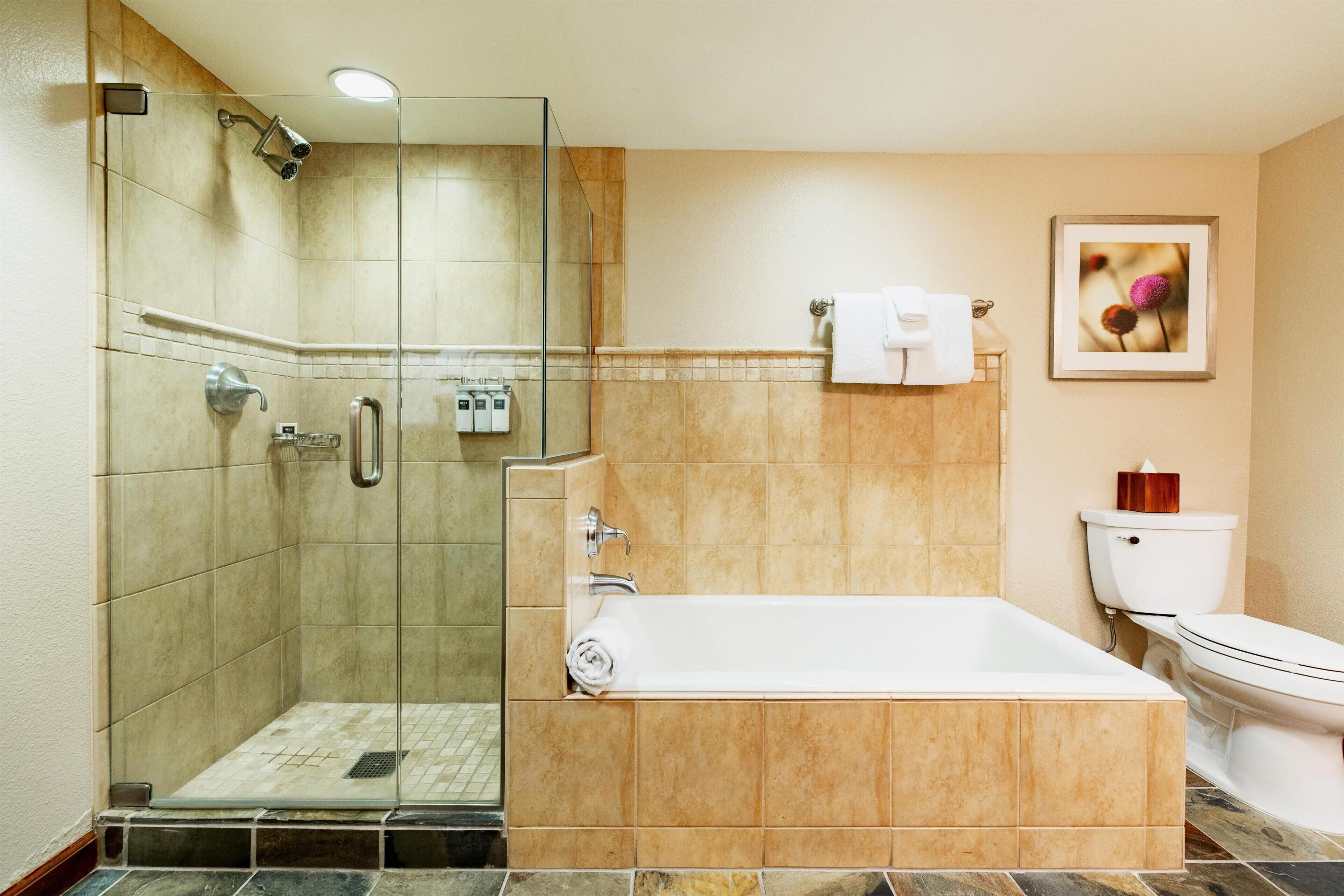A bathroom with a glass-enclosed shower, a bathtub, a toilet, and a framed picture on the wall.
