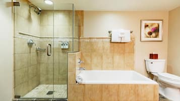A bathroom with a glass-enclosed shower, a bathtub, a toilet, and a framed picture on the wall.