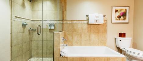 A bathroom with a glass-enclosed shower, a bathtub, a toilet, and a framed picture on the wall.