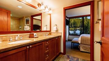 A bathroom with two sinks, a large mirror, and a view of a bedroom through an open door.