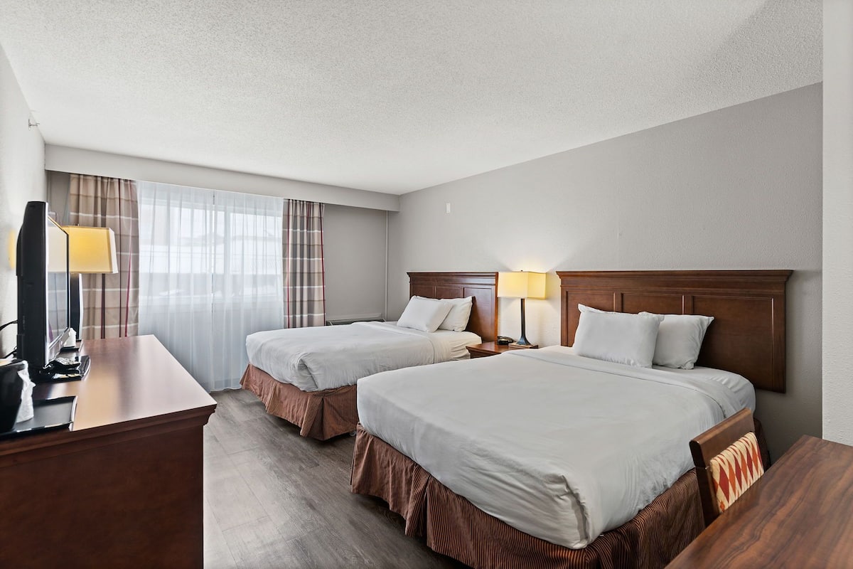 A hotel room with two beds, a desk with a lamp, and a television.