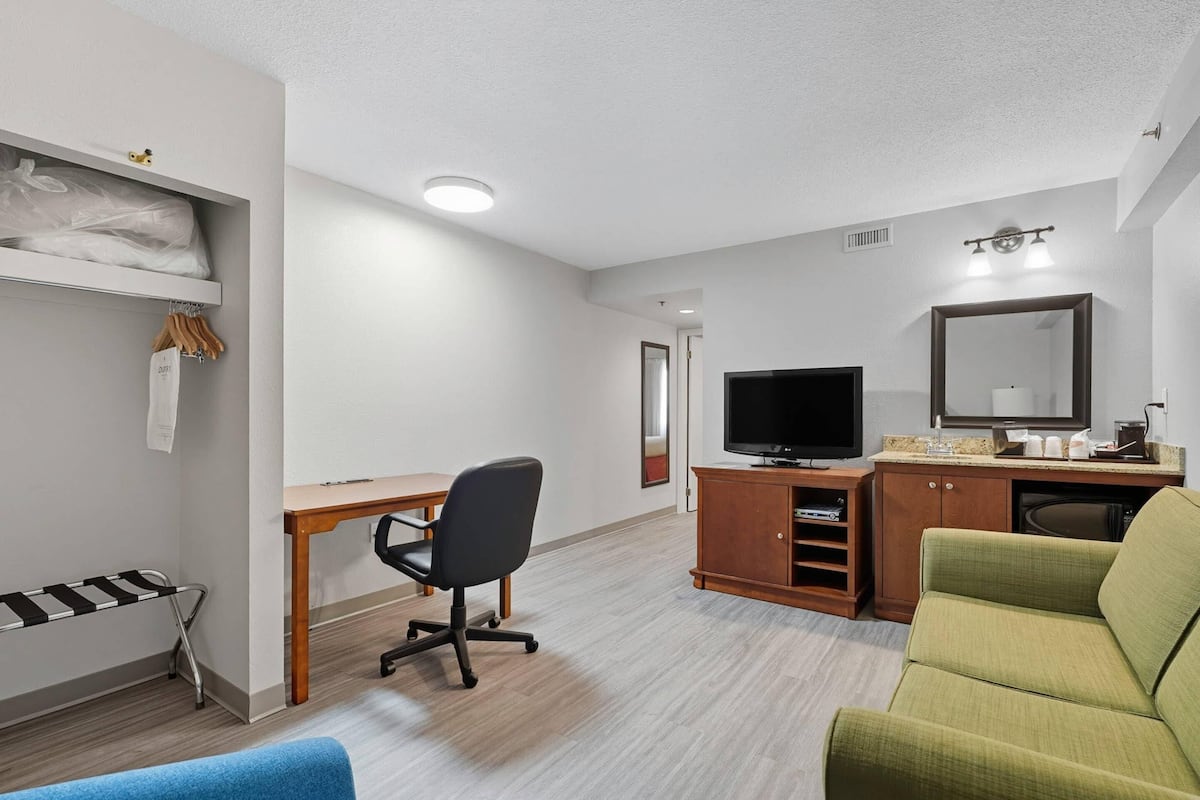 A hotel room with a bed, a desk with a chair, a television, a wardrobe, and a sofa.