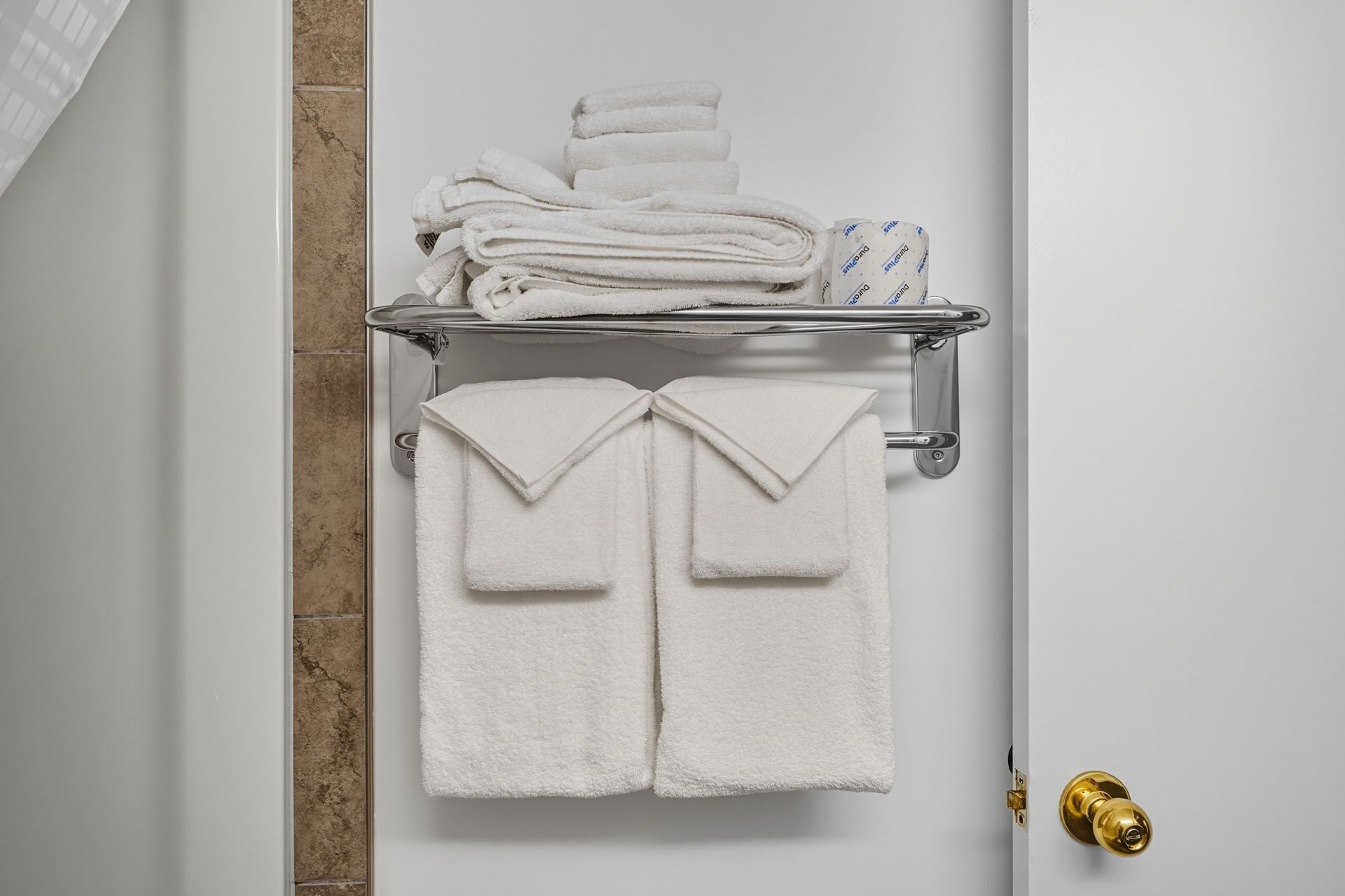 A bathroom with a towel rack holding folded towels and a towel hanging on the wall.