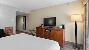 Une chambre d’hôtel avec un lit, un téléviseur posé sur une commode en bois, un bureau avec une chaise et une lampe.