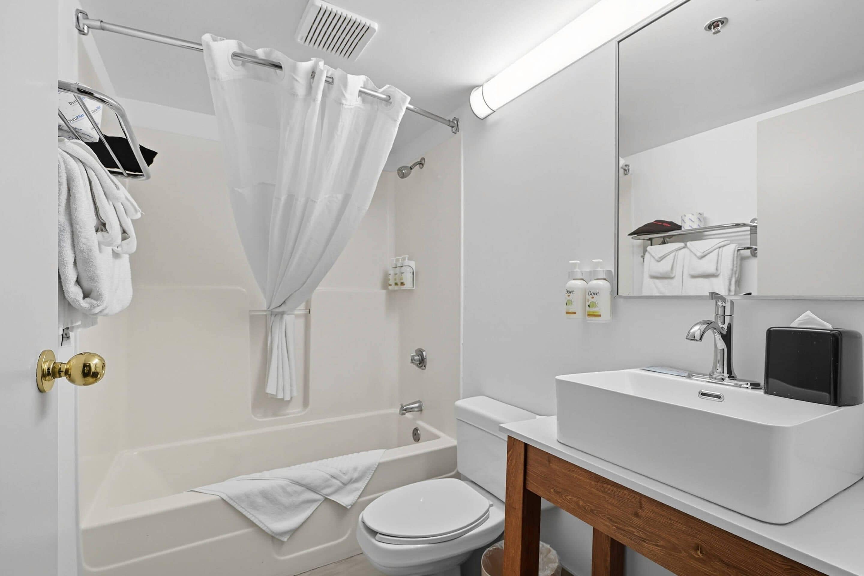 Un baño moderno con bañera, inodoro y lavabo. Se ven toallas y artículos de aseo.