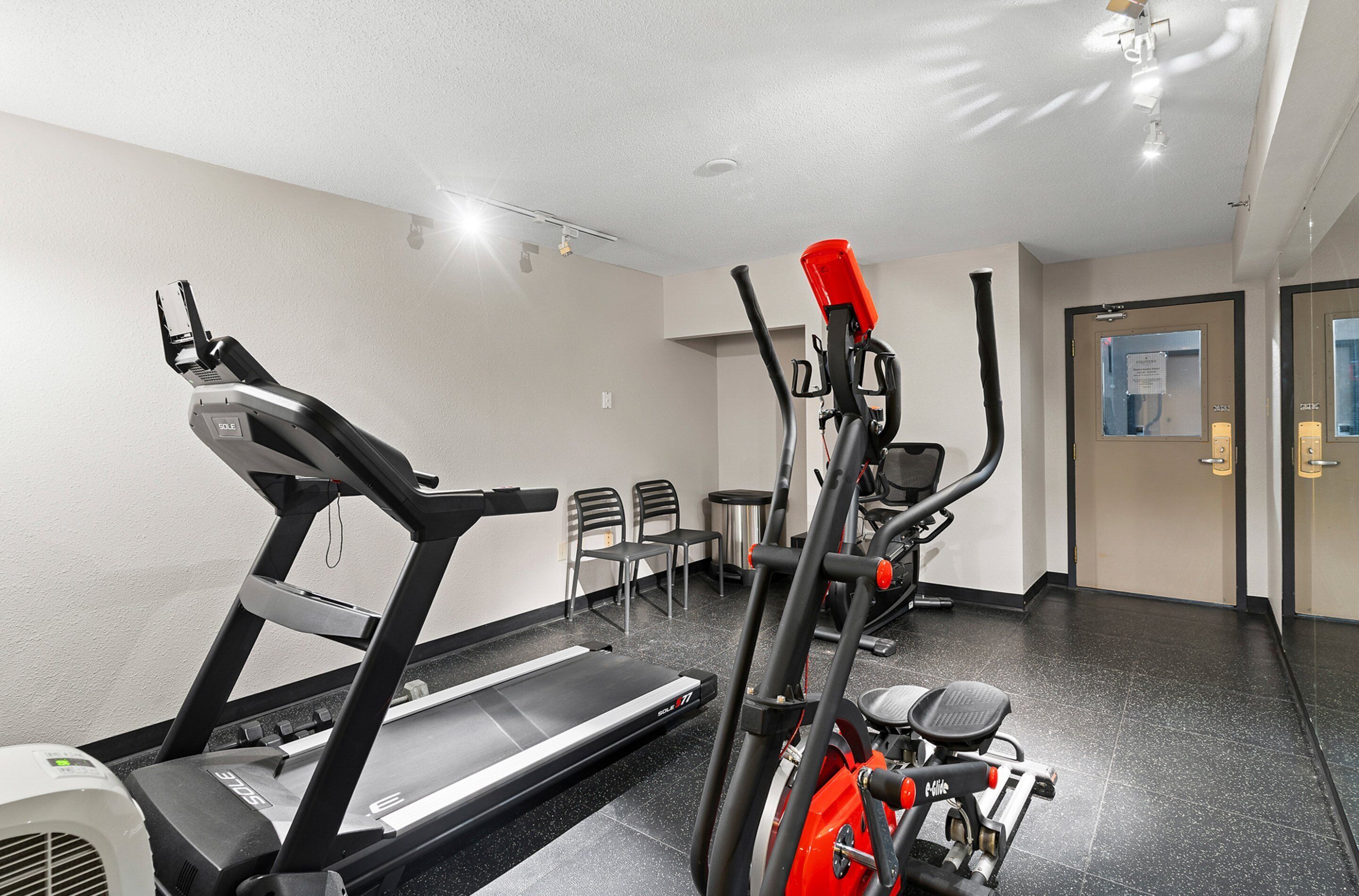 Un gimnasio con caminadora, bicicletas estáticas y sillas.