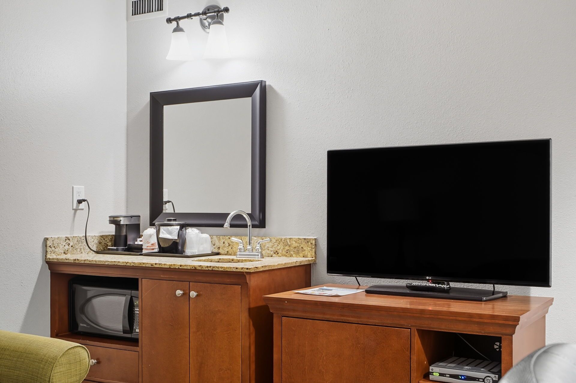 Quarto de hotel com toucador de madeira, um espelho grande, televisão de ecrã plano e um micro-ondas.