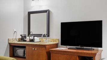 Quarto de hotel com toucador de madeira, um espelho grande, televisão de ecrã plano e um micro-ondas.