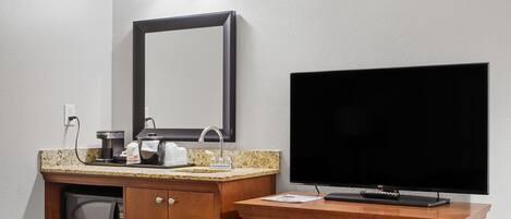A hotel room with a wooden vanity, a large mirror, a flat-screen TV, and a microwave.