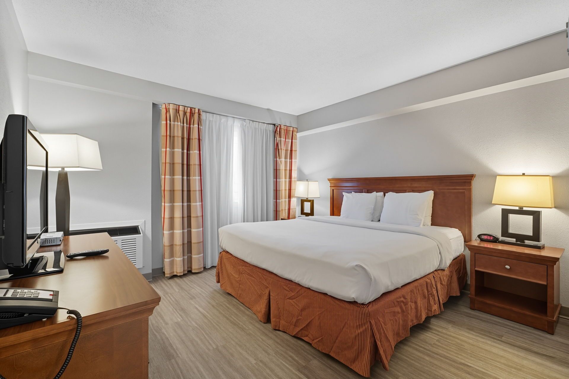 Une chambre d’hôtel comprenant un lit, un bureau avec un téléphone, une télévision et une table de chevet avec une lampe.