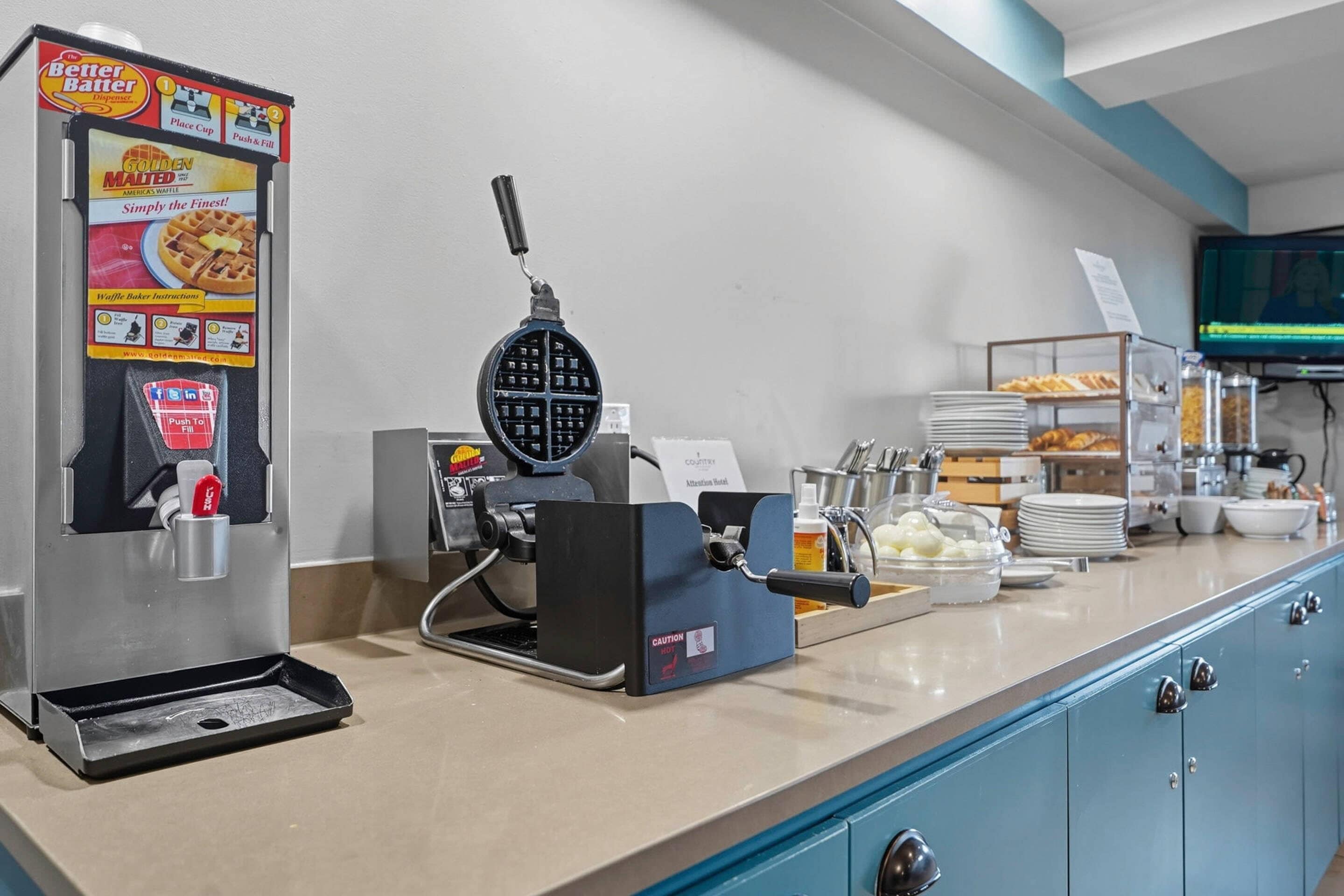 A breakfast bar with a waffle maker, a coffee machine, and various breakfast items.