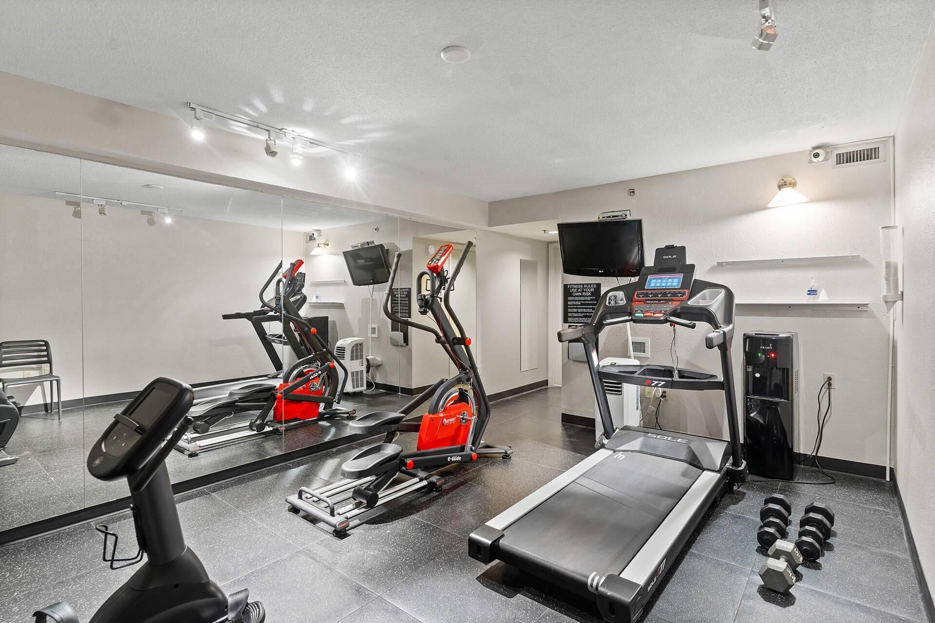 A gym with cardio machines, a treadmill, and dumbbells.