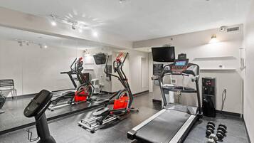 A gym with cardio machines, a treadmill, and dumbbells.