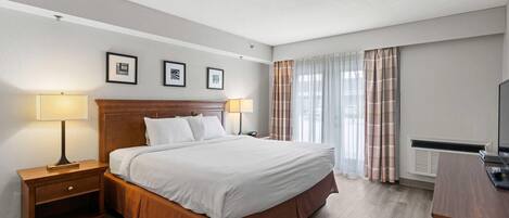 A hotel room with a large bed, two bedside tables with lamps, a flat-screen TV, and a window with curtains.