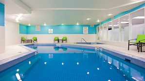 Una piscina interior con carriles claramente delimitados, sillas verdes y suelo de baldosas azules.
