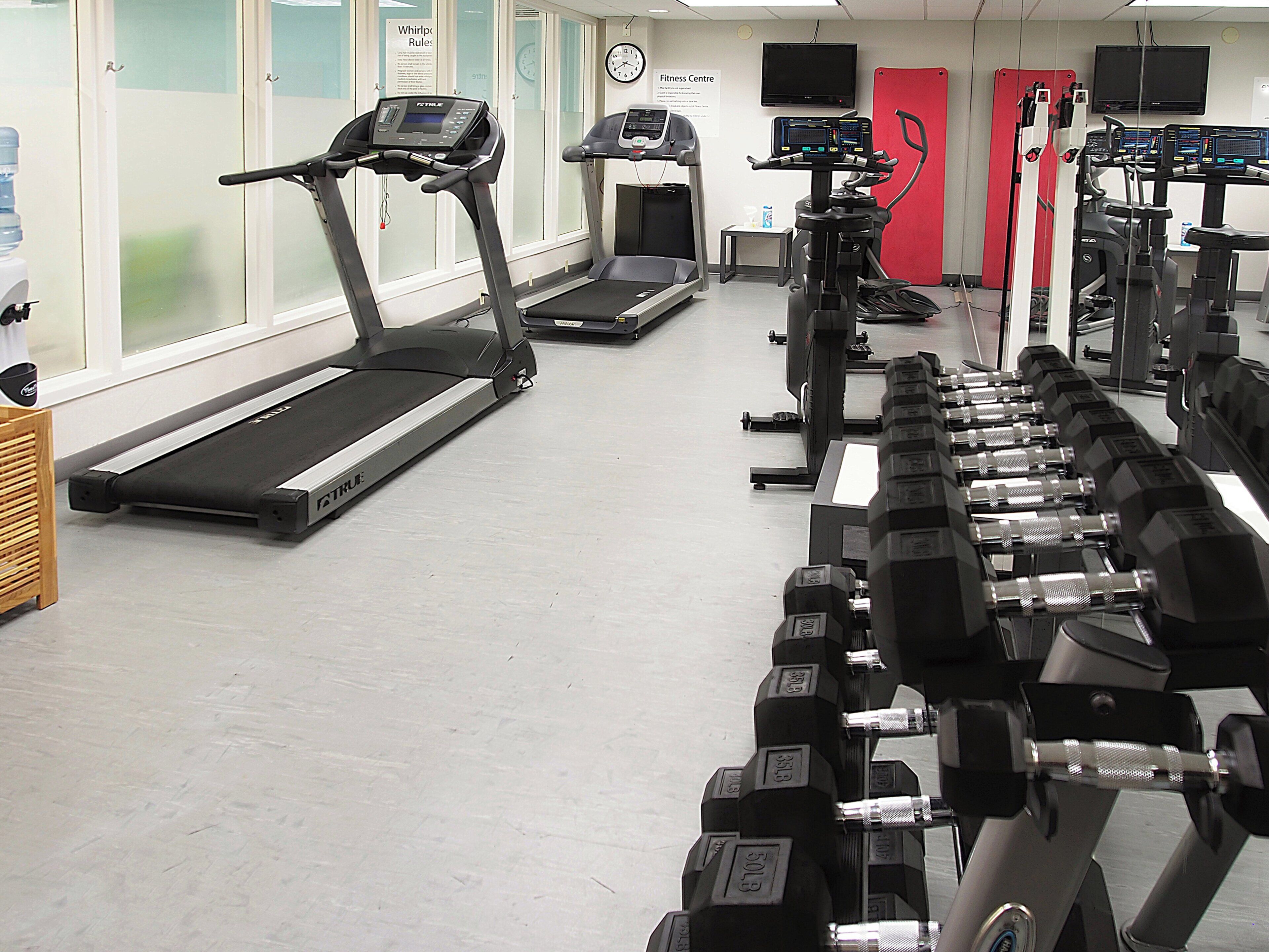 Un gimnasio con cintas de correr, una máquina de escaleras y un juego de mancuernas.