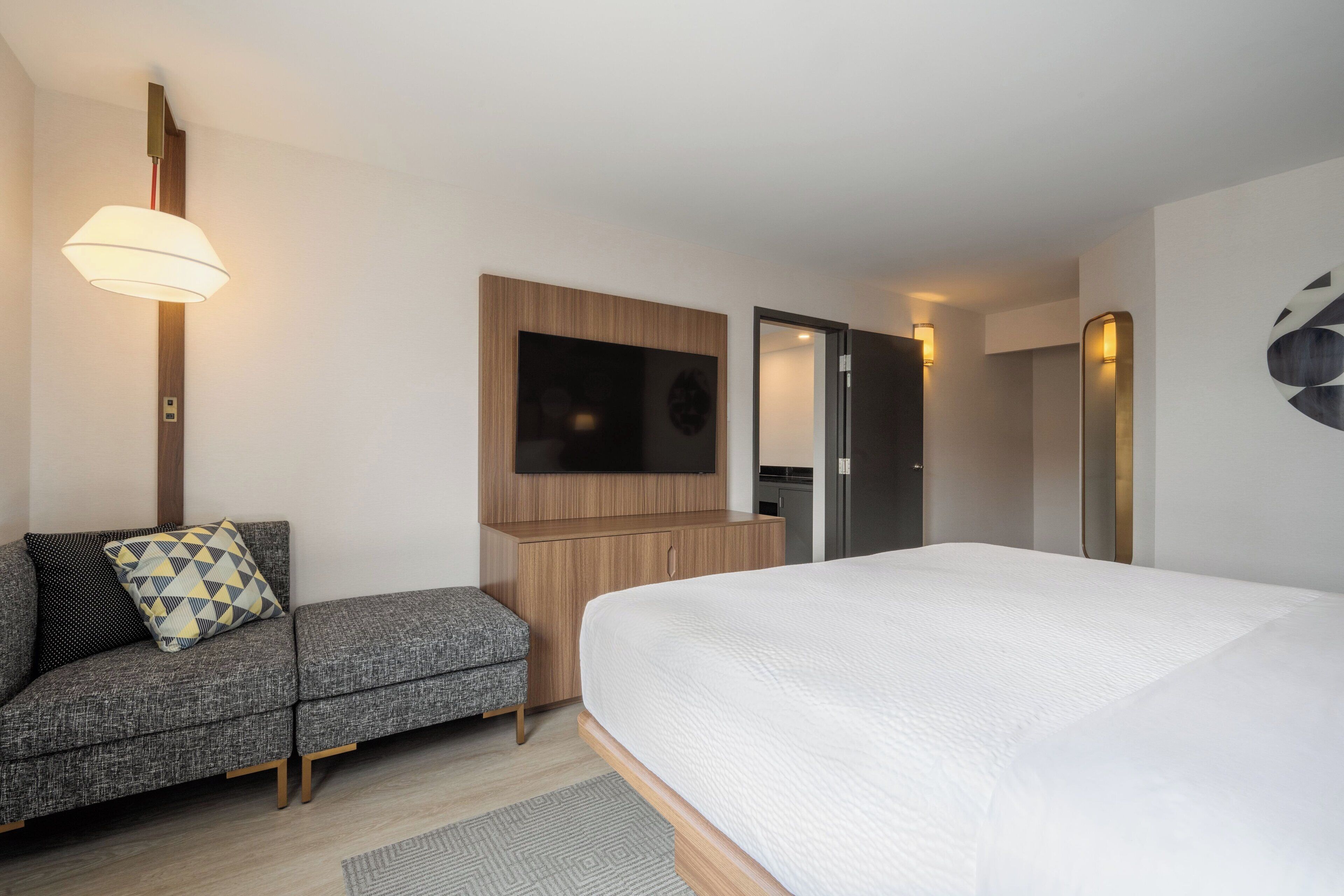 Una habitación de hotel moderna con una cama grande, un sofá, un televisor montado en la pared y un mueble de madera.