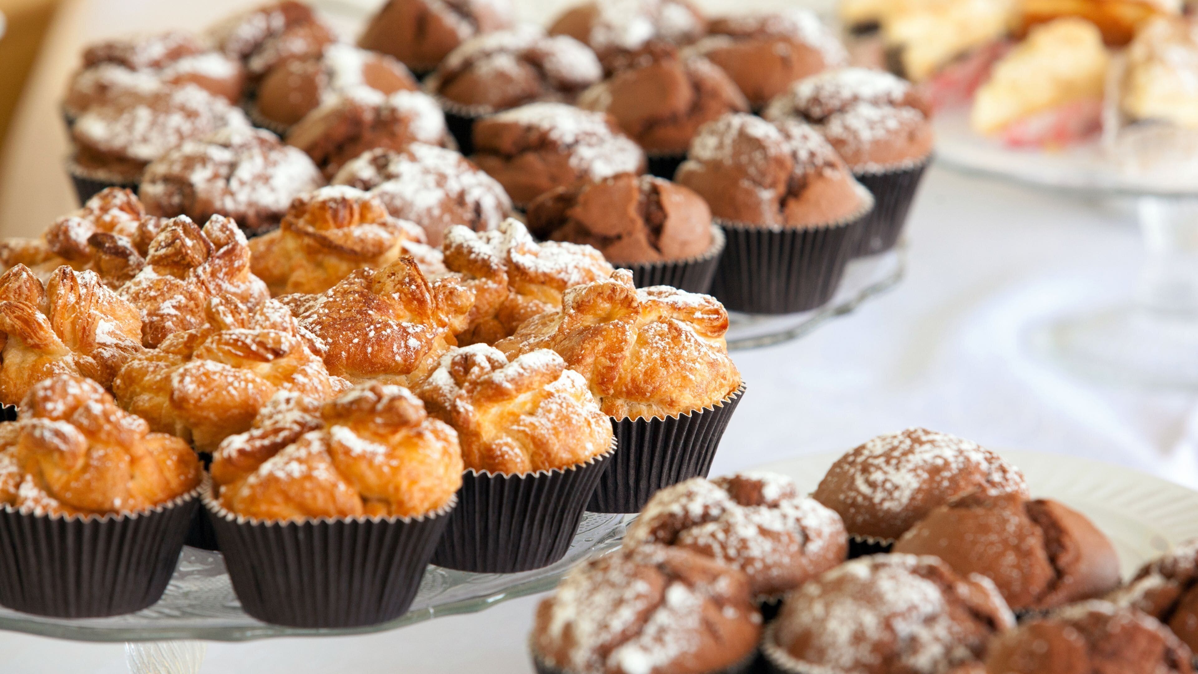 A variety of pastries on display, including muffins and croissants, arranged on a glass stand.