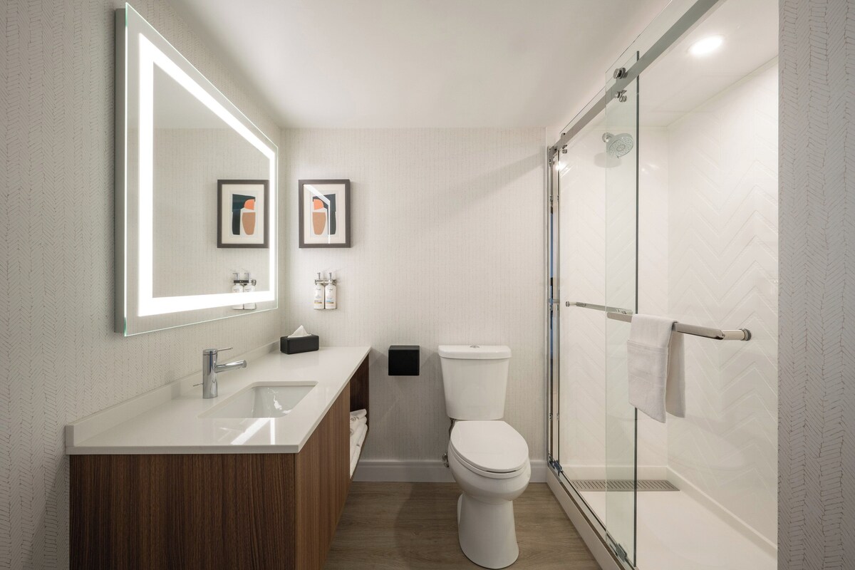 A modern bathroom with a large mirror, a sink, a toilet, and a glass-enclosed shower.
