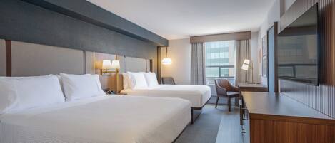 A hotel room with two beds, a desk, a chair, a TV, and a window with curtains.