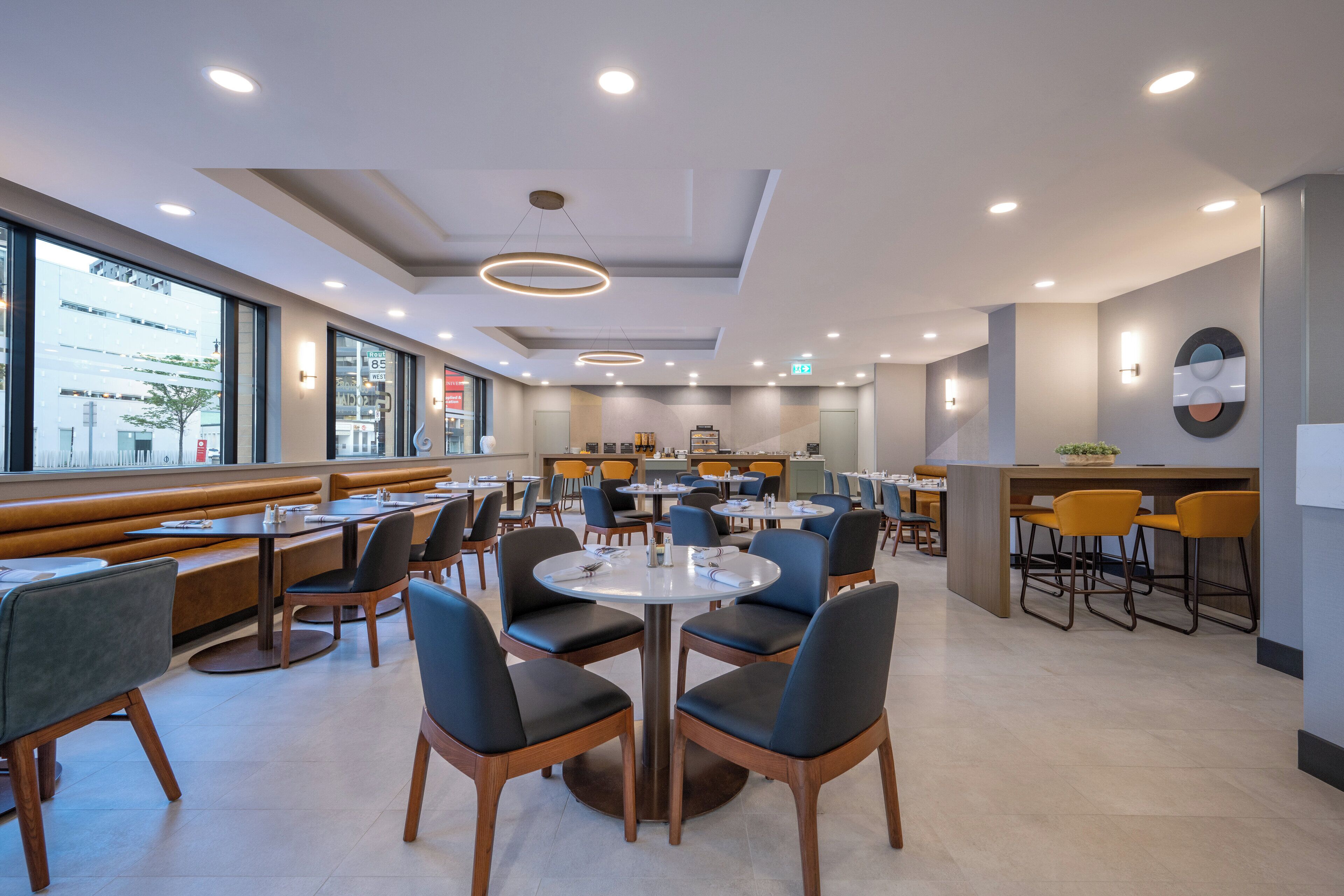 A modern restaurant with round tables, black and wooden chairs, and a view of the city through large windows.