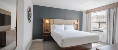 Habitación de hotel con una cama grande, lámparas de noche, mesita de noche, un espejo y vista a la ciudad por la ventana.
