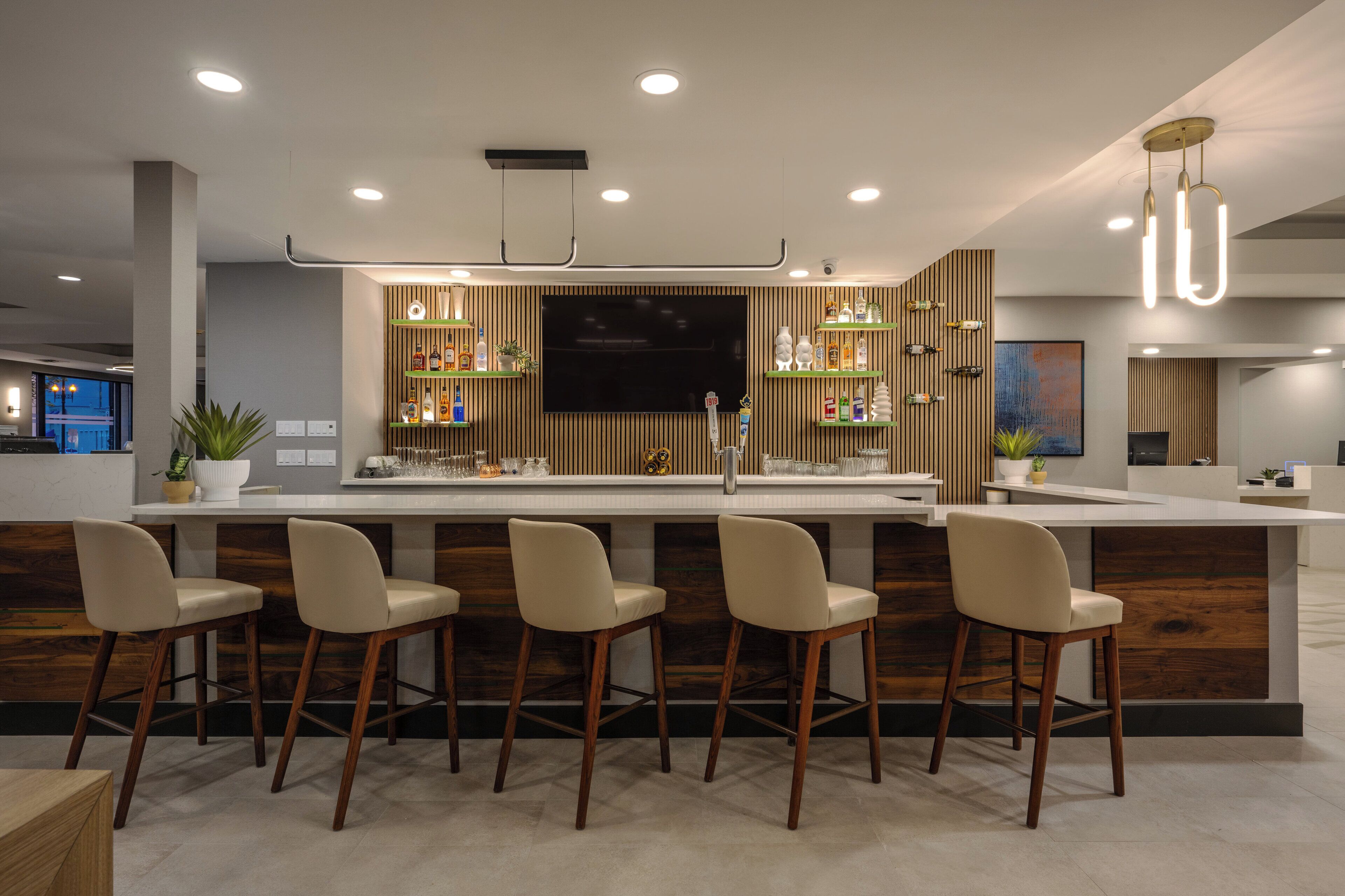 A modern kitchen with a central island, bar stools, wooden paneling, and built-in shelving with kitchen items.