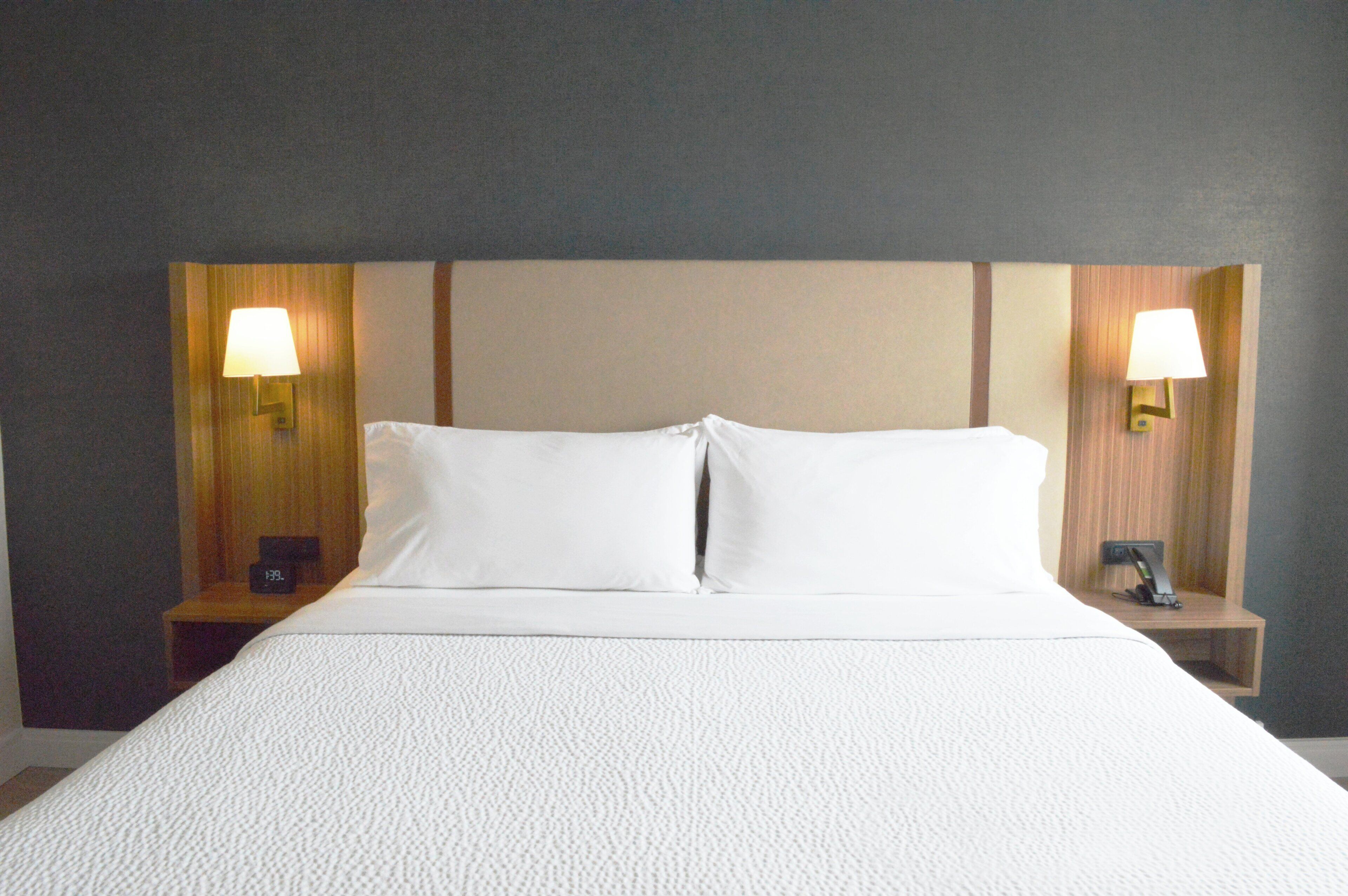 A neatly made bed with white linens, two bedside tables with lamps, and a wall with a wooden panel design.
