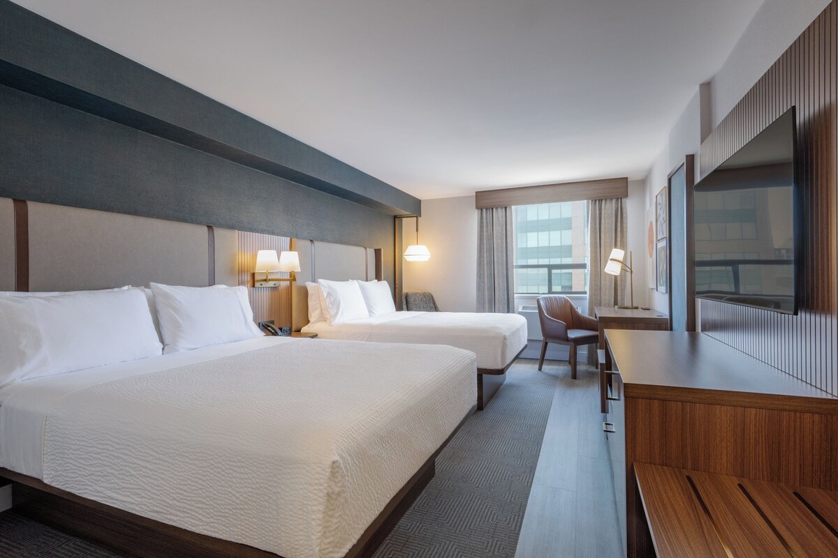 A hotel room with two beds, a desk, a chair, a TV, and a window with curtains.