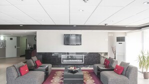 Un salon moderne avec des canapés gris, un mur d’accent rouge, un téléviseur à écran plat et une cheminée.