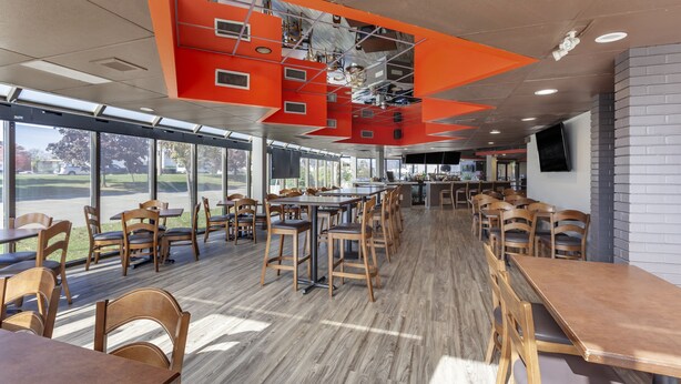 Un vaste espace dédié à la salle à manger, doté de hauts plafonds, de grandes fenêtres et d’un design moderne agrémenté de touches de couleur orange.