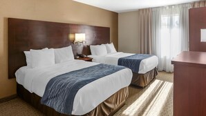 Une chambre d’hôtel avec deux lits, une tête de lit en bois, une table de chevet avec une lampe et une vue sur l’extérieur par une fenêtre avec des rideaux.