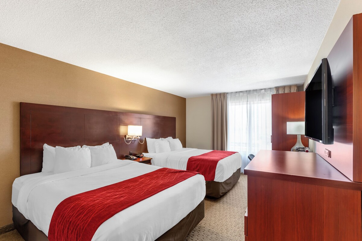 A hotel room with two beds, a desk, a television, and a window with curtains.
