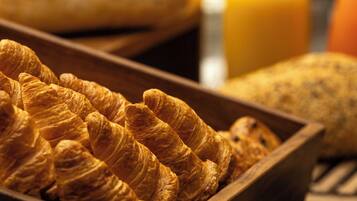 A wooden tray filled with croissants and a loaf of bread, with a glass bottle of orange juice in the background.
