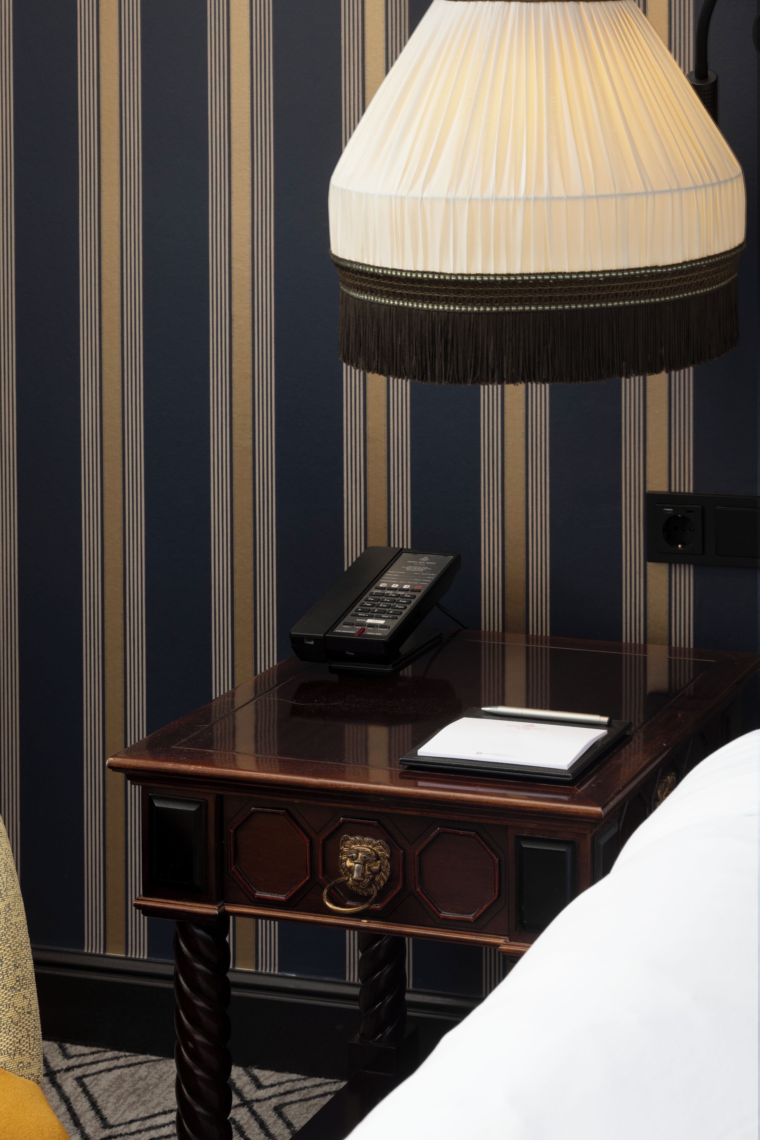 Une chambre d’hôtel avec une table de chevet en bois, un téléphone et un bloc-notes.