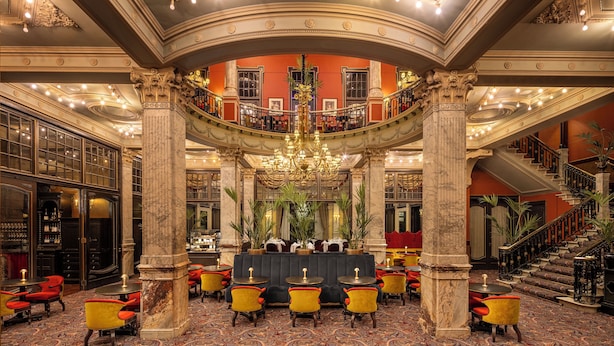 Un lobby imponente con columnas decoradas, un bar en el centro y una escalera que sube a los pisos superiores.