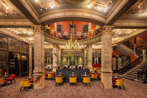 A grand lobby with ornate columns, a central bar area, and a staircase leading to upper floors.