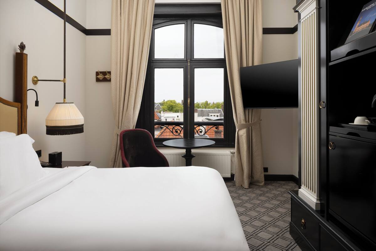 Une chambre d’hôtel avec un lit, une télévision, une table et une fenêtre avec des rideaux.