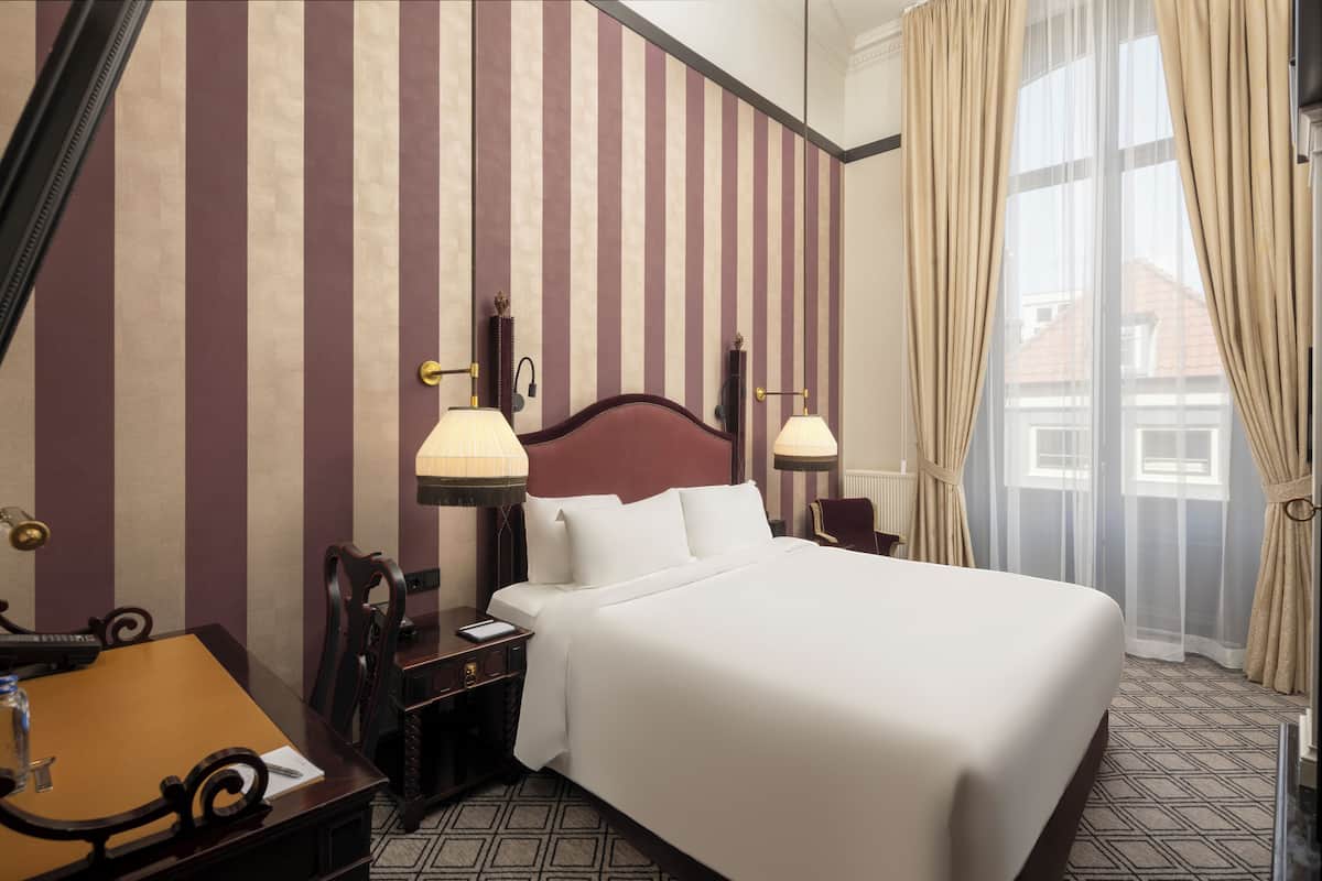 Une chambre d’hôtel avec un grand lit, deux lampes de chevet, une table de chevet, un bureau en bois et une chaise.