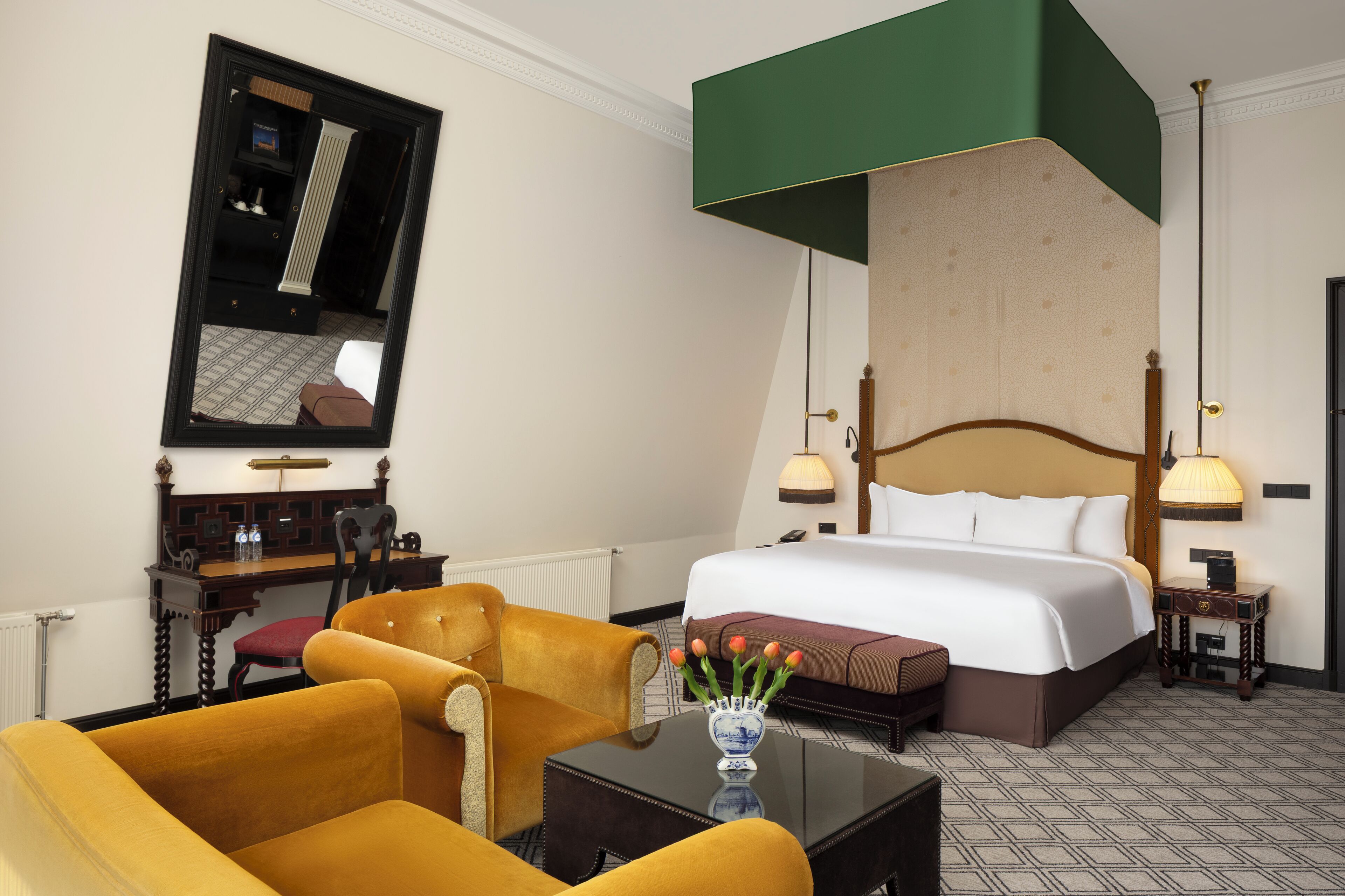 Een hotelkamer met een groot bed, een bureau met stoel, een spiegel en een vaas met bloemen.