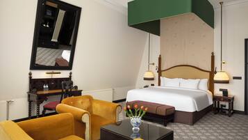 Una habitación de hotel con una cama grande, un escritorio con silla, un espejo y un florero con flores.