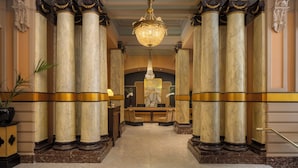 Un lobby imponente con columnas de mármol, un candelabro y una mesa de recepción.