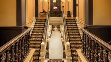 A grand staircase with ornate railings and carpeted steps leading to a landing with a chandelier.