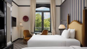 A hotel room with a large bed, a desk, two chairs, a TV, and a window with curtains.