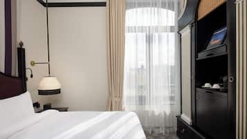 Una habitación de hotel con una cama, una mesita de noche, una lámpara, un armario y cortinas traslúcidas.