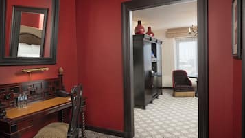 Habitación de hotel con pared roja, un escritorio de madera con silla, un armario y un espejo.