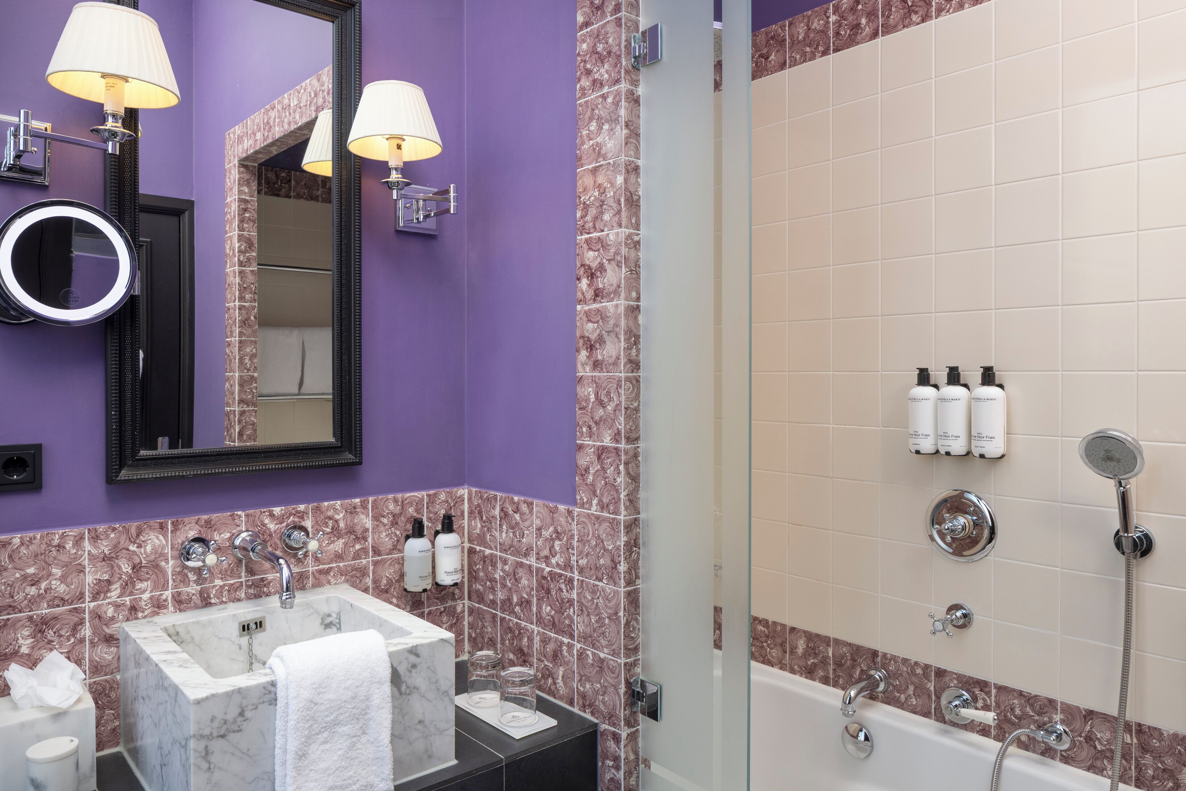 A bathroom with a purple wall, a marble sink, a large mirror, and a glass-enclosed shower area.