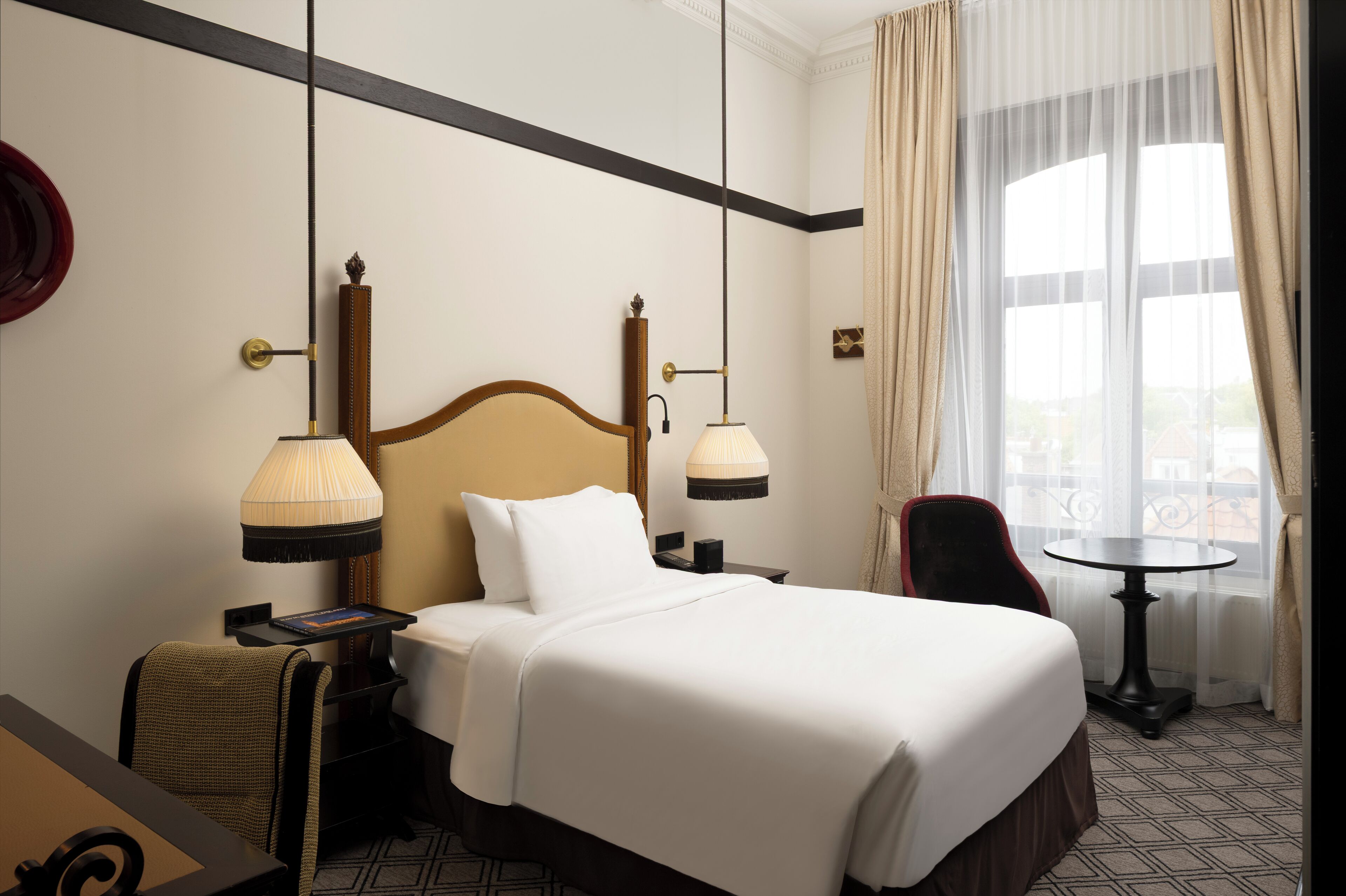 Ett hotellrum med en stor säng, två sänglampor, ett litet bord, en stol och utsikt över omgivningarna genom stora fönster.